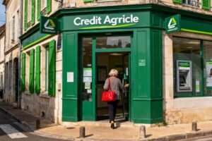 Femme entrant dans l'agence Crédit Agricole de Langeais avec sac à main rouge devant une façade traditionnelle française