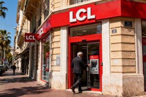 Façade moderne de l'agence LCL avec logo rouge vif, un homme d'affaires entrant dans la banque sous le soleil niçois