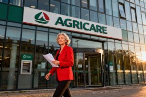 Siège social du Crédit agricole à Vannes avec façade vitrée moderne et femme d'affaires en veste rouge marchant vers l'entrée