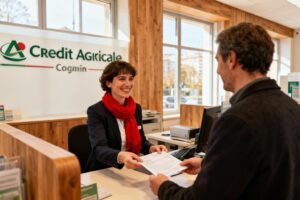 Conseiller bancaire souriant aidant un client devant le comptoir d'une agence Crédit Agricole avec documents