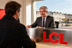 Conseiller LCL aidant un client au comptoir dans une agence moderne, avec vue sur Dieppe en arrière-plan