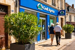 Façade de l'agence Crédit Agricole à La Châtre avec plantes vertes et enseigne bleue, un couple âgé entre dans la banque